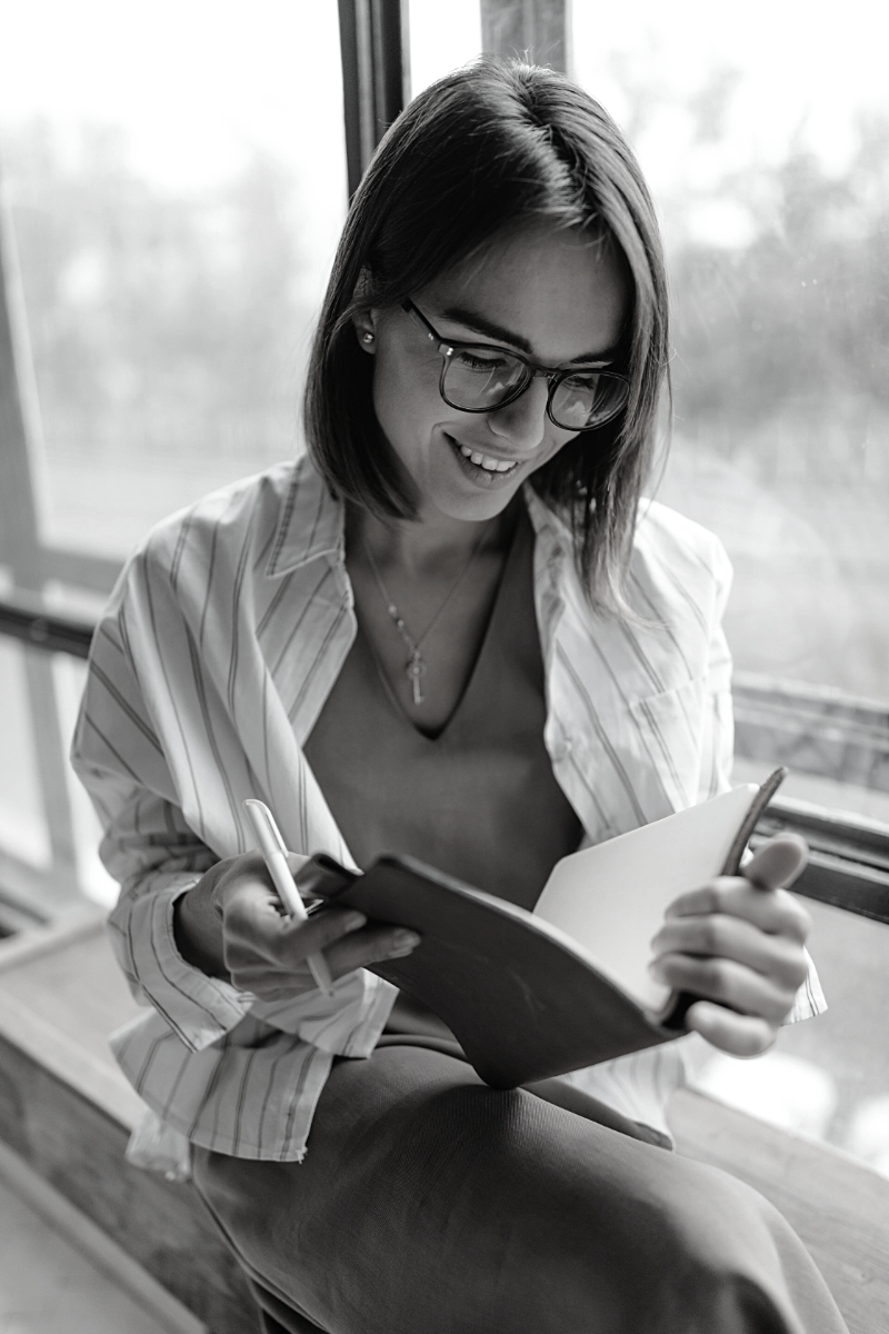 Image shows a woman who is smiling and reading a book.